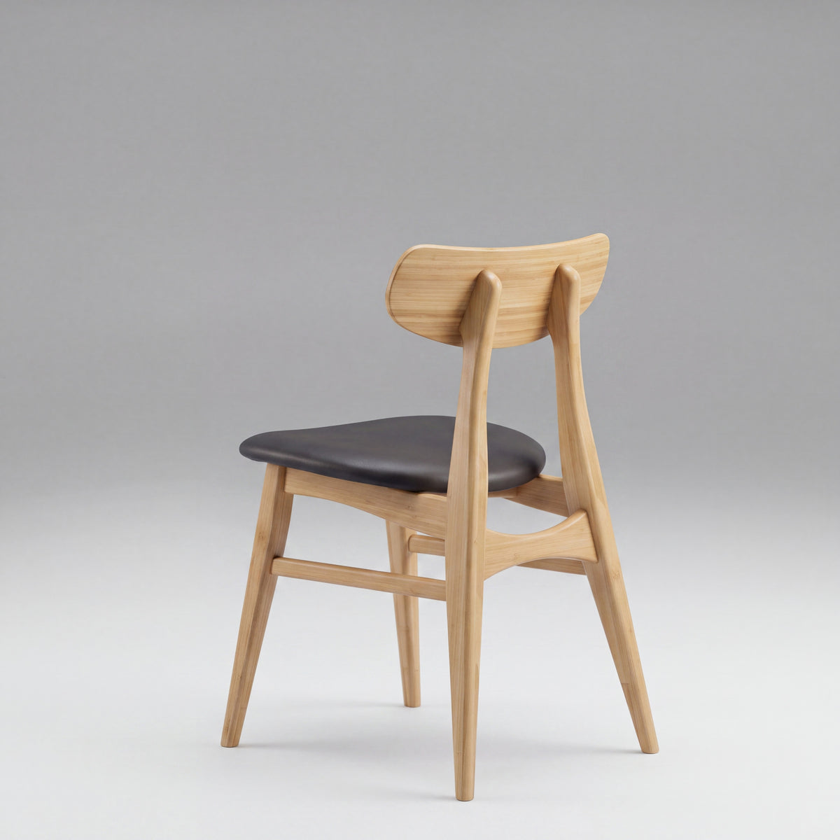 Greenington Cassia Dining Chair in Caramelized bamboo with a black leather seat, on a grey studio background, rear three-quarter view