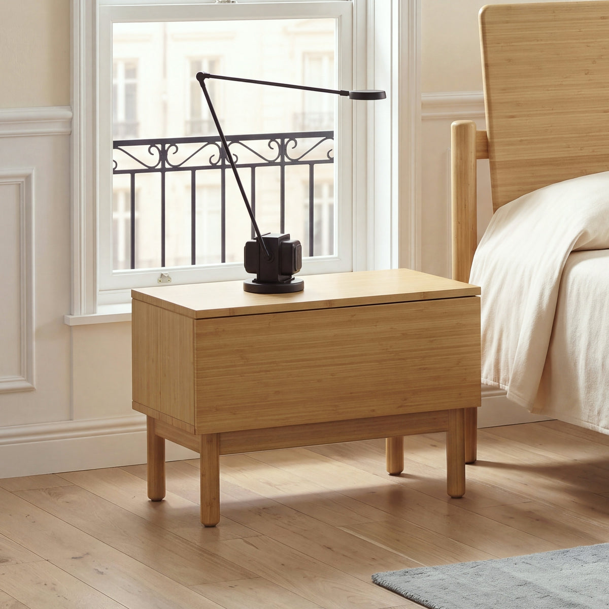 Monterey Nightstand in Wheat bamboo with a black arc lamp in front of a tall sash window with an iron balcony rail