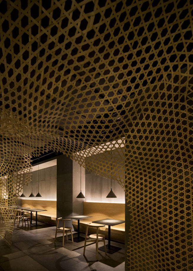Restaurant interior with a honeycomb-pattern ceiling over wood dining tables